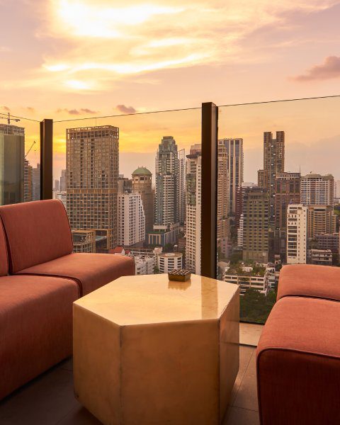 Comfortable sofa unit and hexagon table on a rooftop bar next to a glass fence overlooking a big city