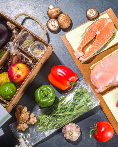The ingredients of a meal delivery kit displayed on a black surface. Some recipe papers are lying on top of the box.