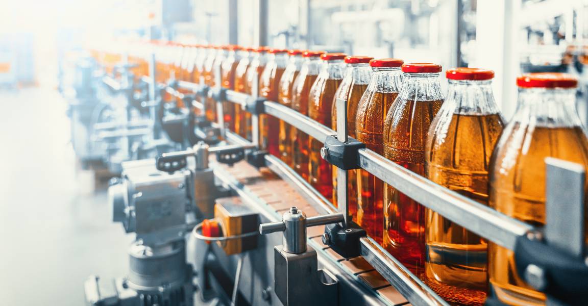 A conveyor belt in a beverage manufacturing facility with glass bottles containing juice. Custom filtration improved quality.